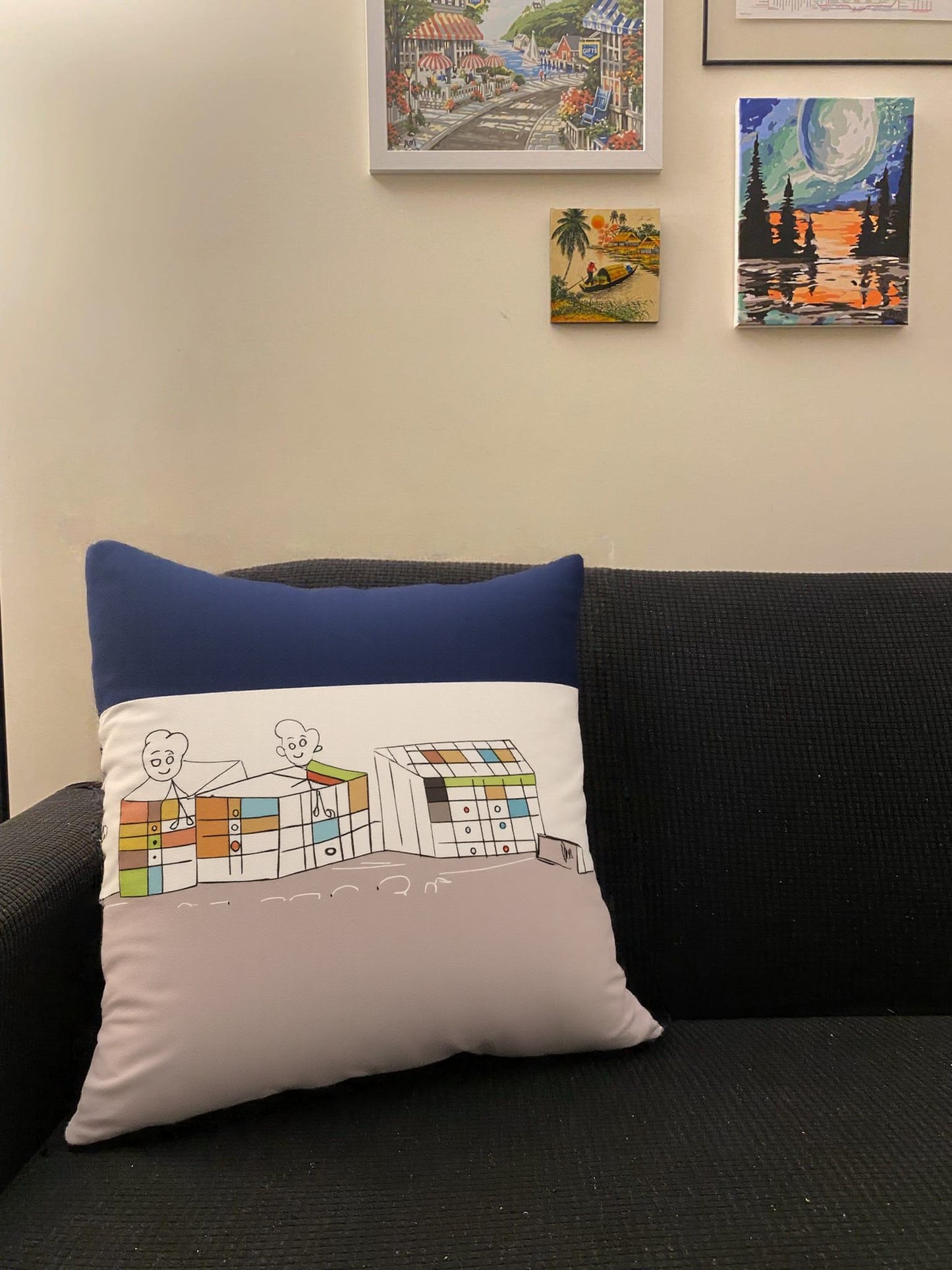 Decorative pillow with a design on a black couch, surrounded by framed artworks on the wall.