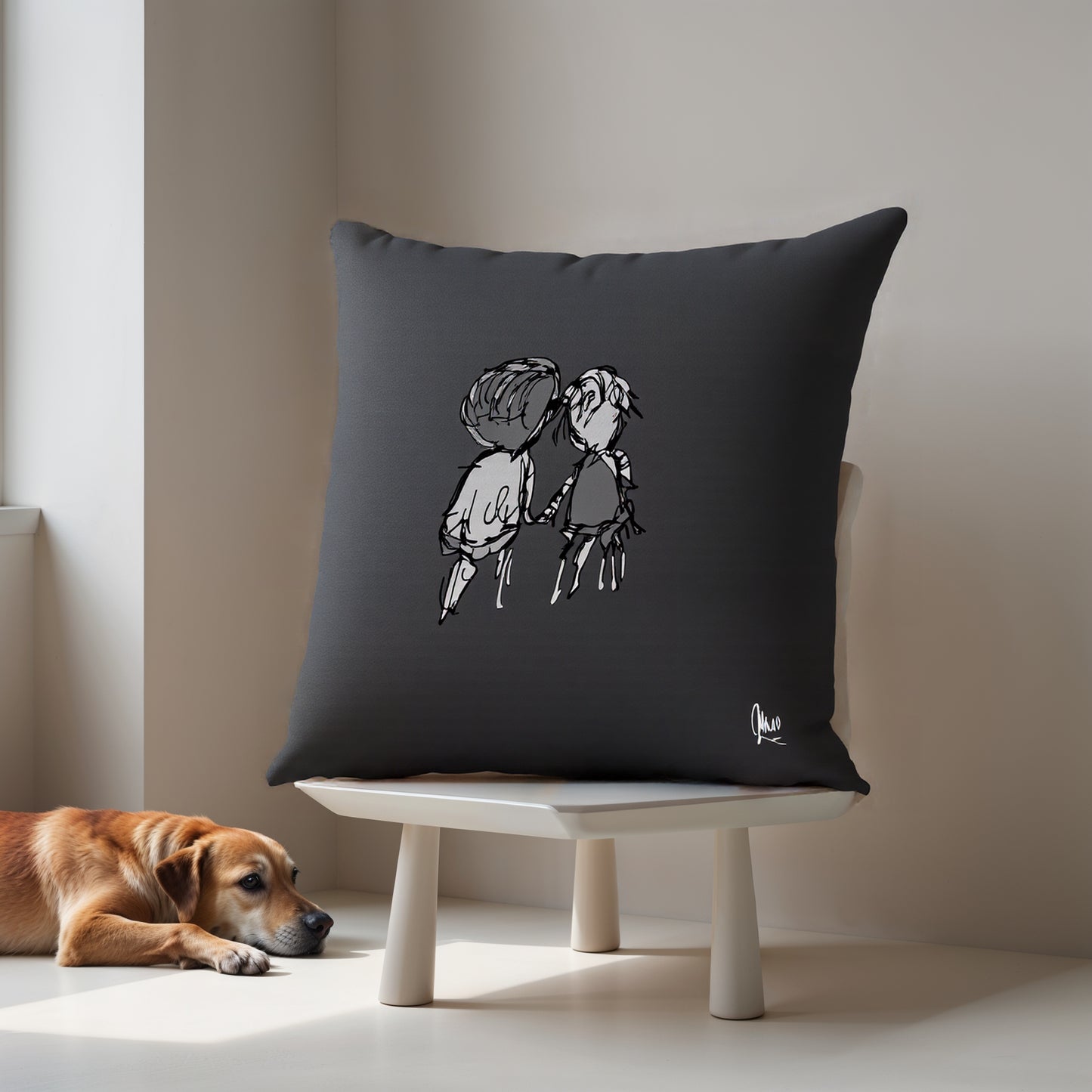 Black pillow with a design of two people holding hands on a white stand, with a dog lying on the floor in the background.