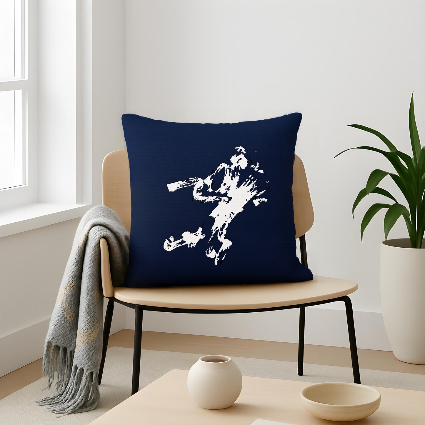 Navy blue pillow with white graphic on a wooden chair in a room with a plant and window - by Northwind Illustrations