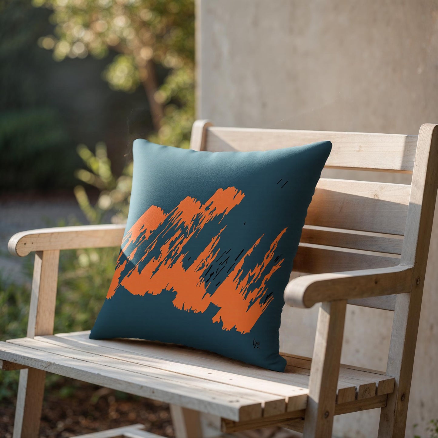 Teal pillow with orange abstract design on a wooden bench outdoors