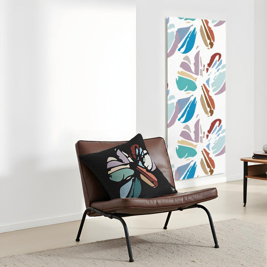 Brown chair with black pillows featuring colorful butterfly designs, against a white wall with a floral abstract painting.